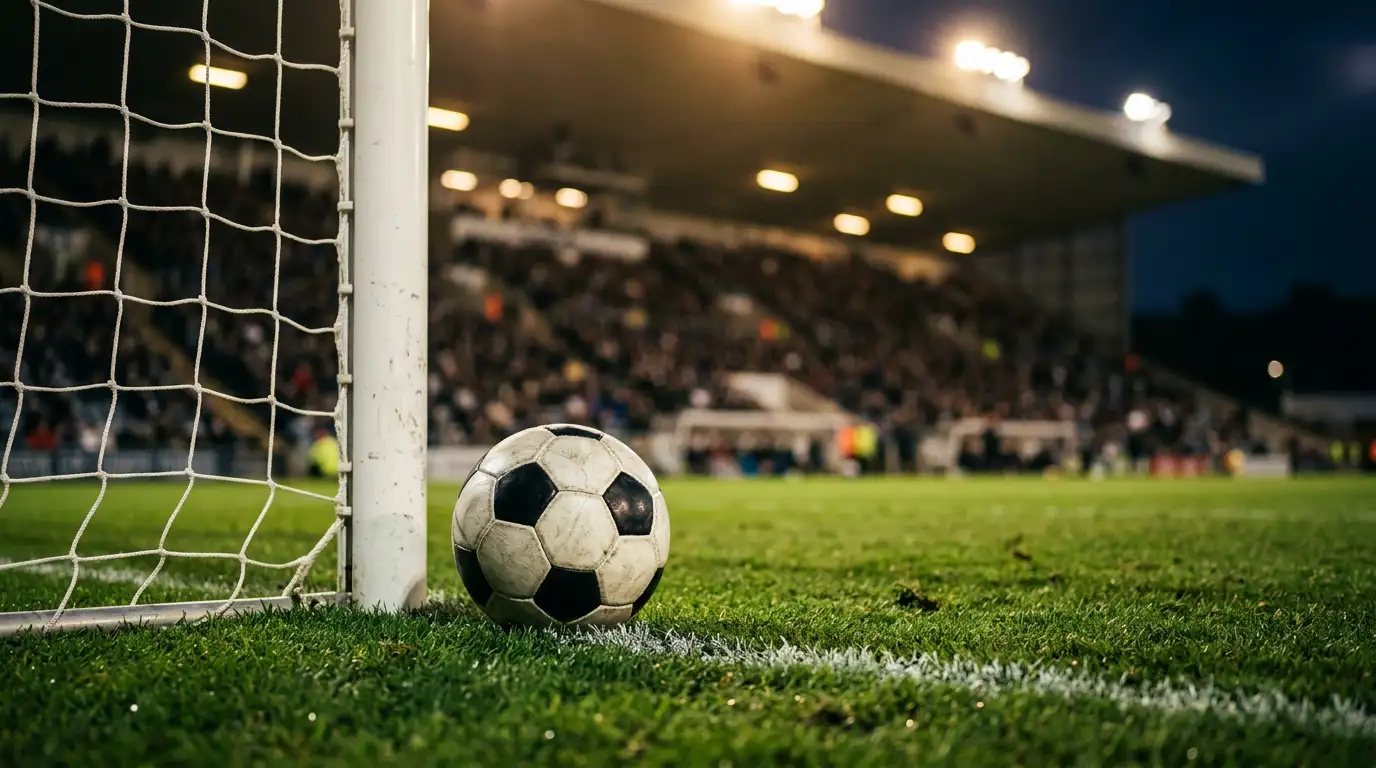 Fotbalová branka se sítí a míčem na zeleném hřišti při večerním osvětlení